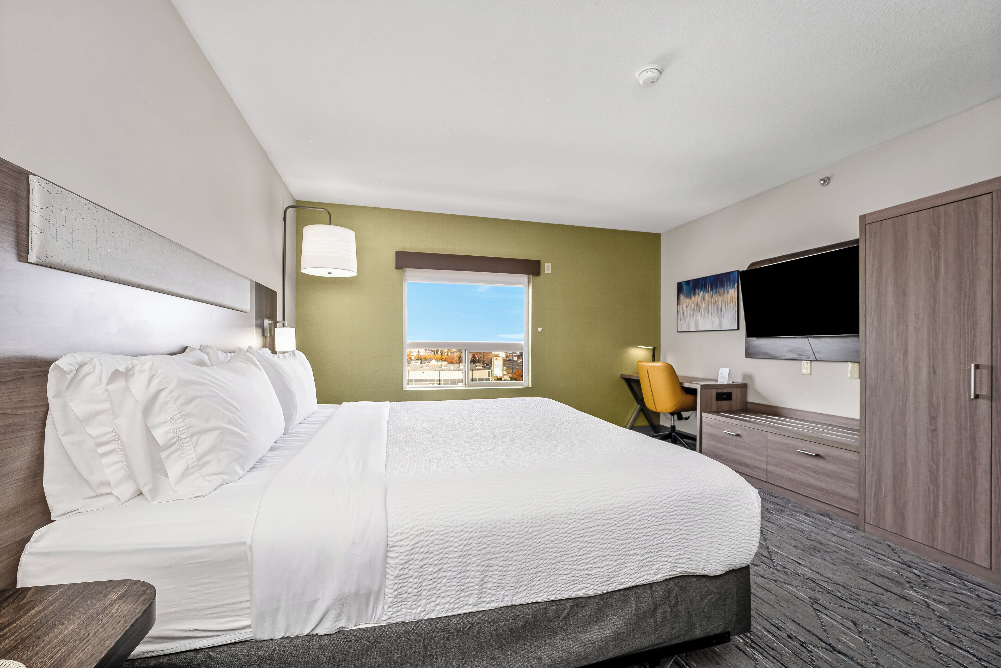 A hotel room with a large bed, a desk, a chair, a TV, and a window with a view.