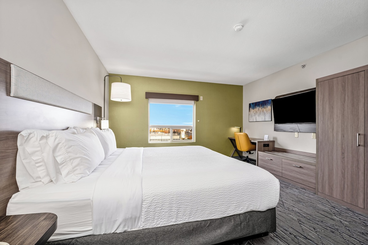 Une chambre d’hôtel avec un grand lit, un bureau, une chaise, une télévision et une fenêtre donnant sur un beau paysage.