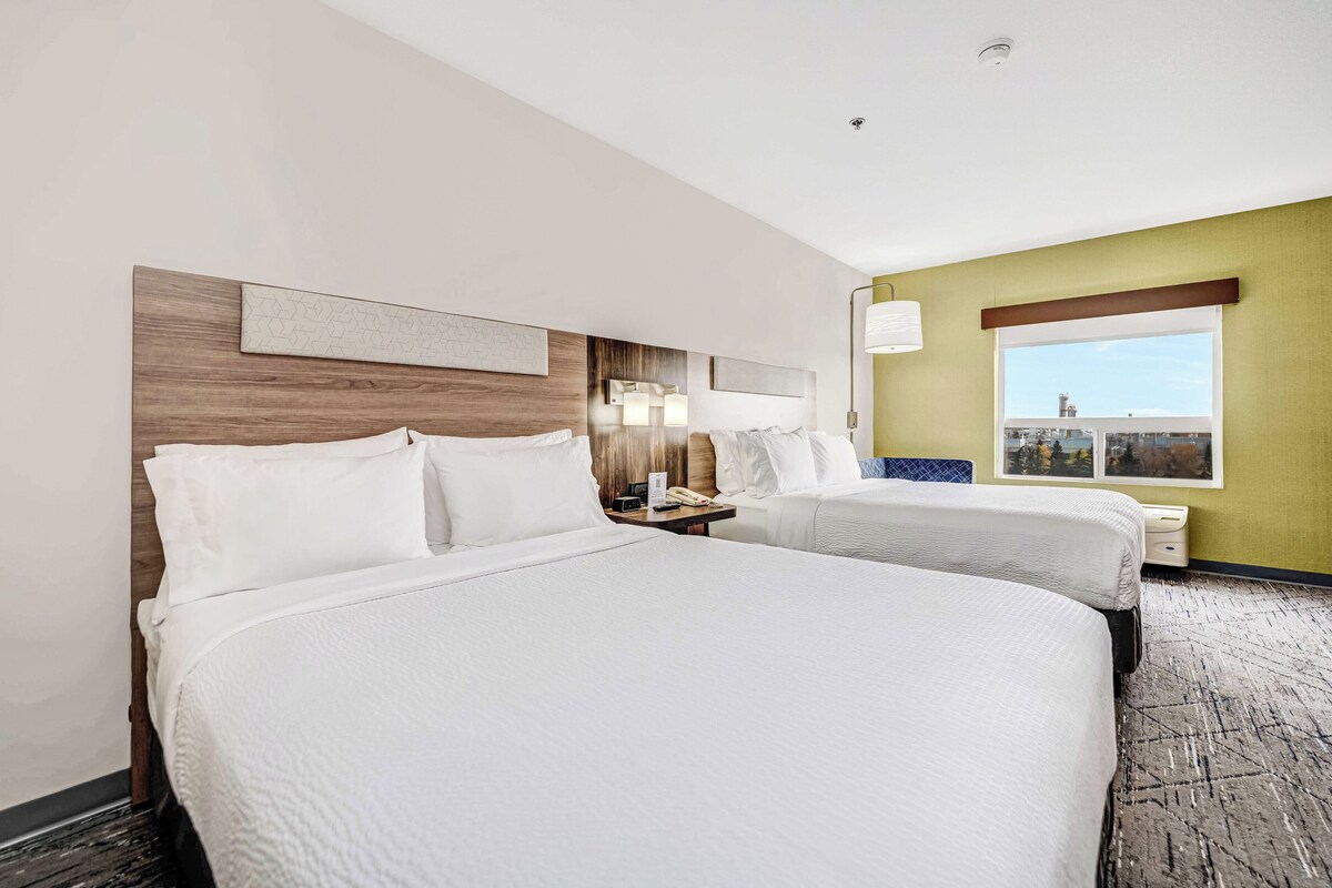 Une chambre d’hôtel avec deux lits, une tête de lit en bois, une table de chevet avec une lampe, une fenêtre donnant sur un paysage agréable et une œuvre d’art accrochée au mur.