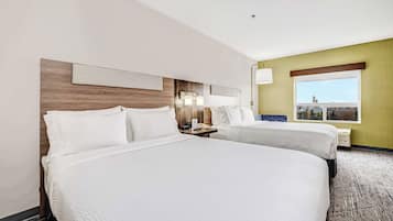 A hotel room with two beds, a wooden headboard, a nightstand with a lamp, a window with a view, and a wall-mounted artwork.