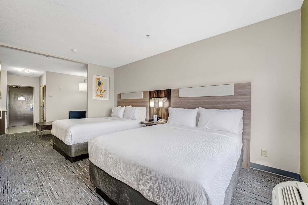 A hotel room with two beds, a desk, a chair, a lamp, and a wall-mounted TV.