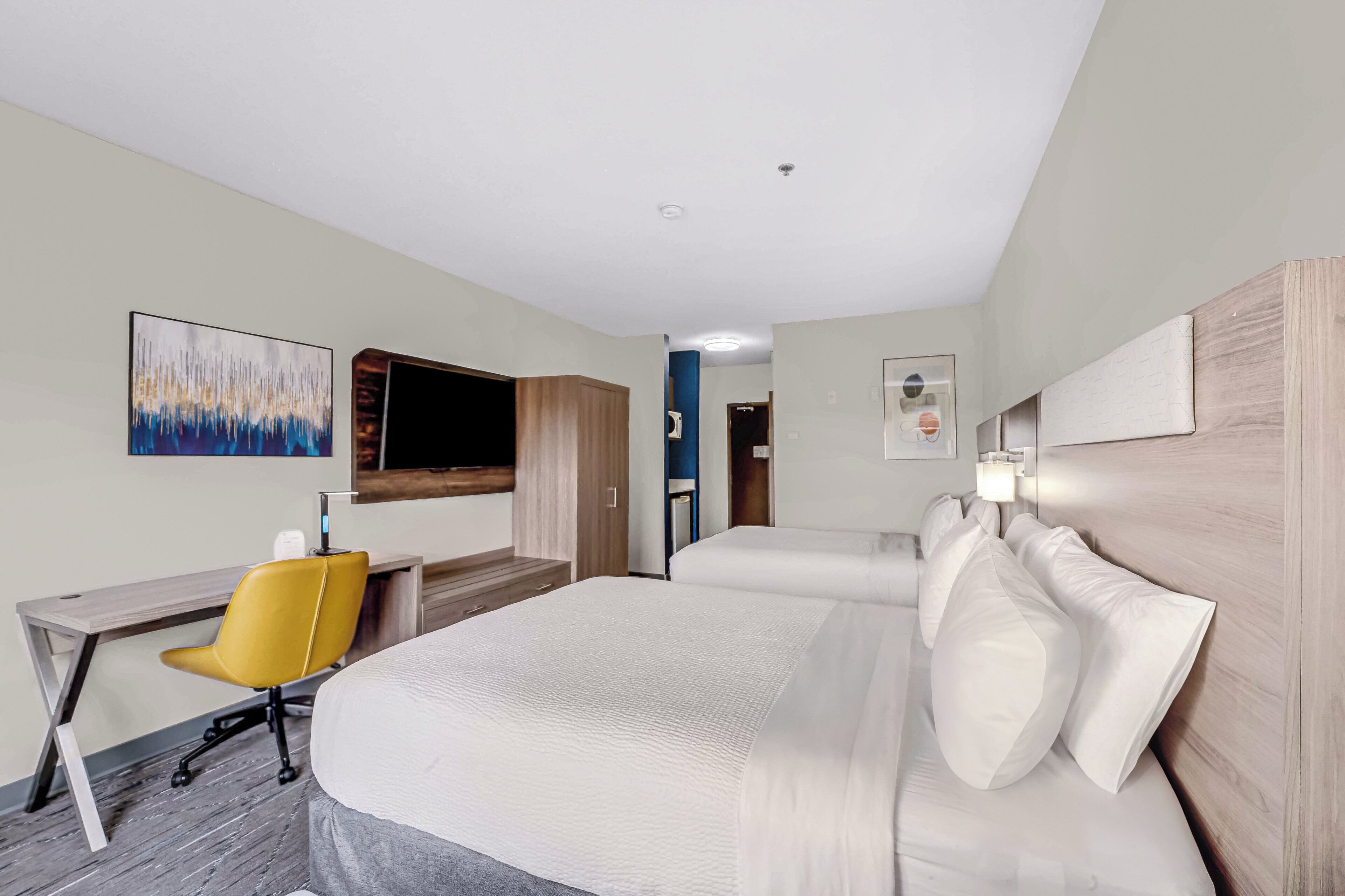 A hotel room with a large bed, a desk with a chair, a TV, and artwork on the walls.