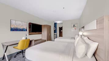 A hotel room with a large bed, a desk with a chair, a TV, and artwork on the walls.