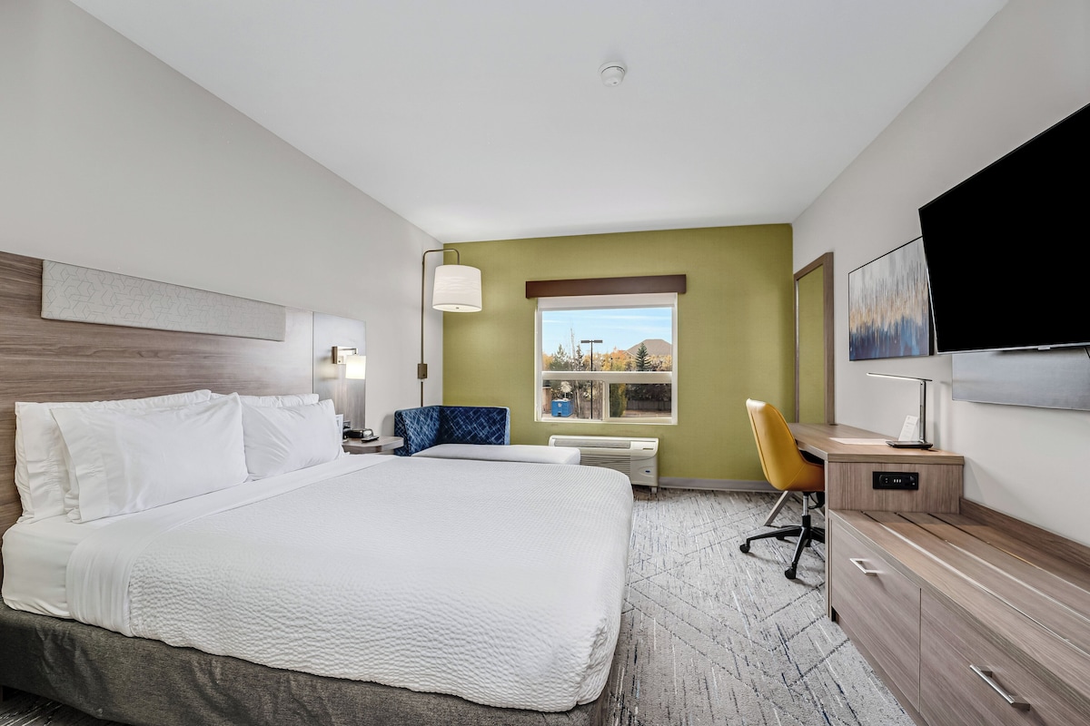 Une chambre d’hôtel avec un grand lit, un bureau avec une chaise, une télévision et une fenêtre donnant sur un beau paysage.