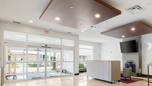 A spacious lobby with a large glass door entrance, a flat-screen TV mounted on the wall, and a seating area with patterned chairs. - Holiday Inn Express Hotel & Suites Edmonton South by IHG (Edmonton)