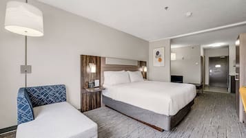 Une chambre d’hôtel comprenant un lit, une chaise, une table de chevet, une lampe et une porte donnant sur une salle de bain.