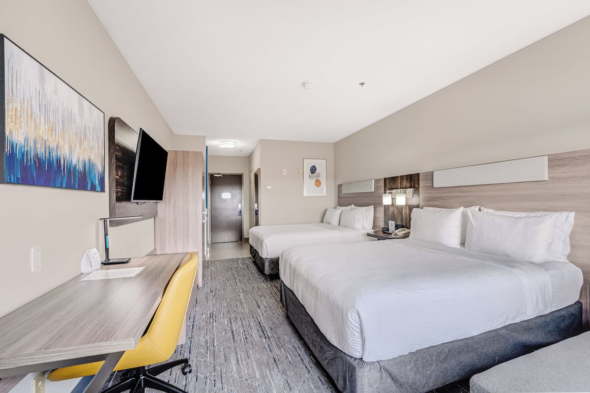 A hotel room with a desk, two beds, a TV, and a painting on the wall.