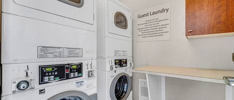A guest laundry area with multiple washing machines, operating instructions, and a wooden panel on the wall.