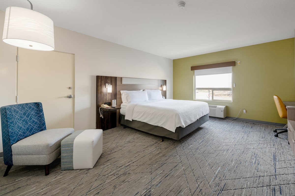 A hotel room with a bed, a desk, a chair, a bedside table, and a lamp.
