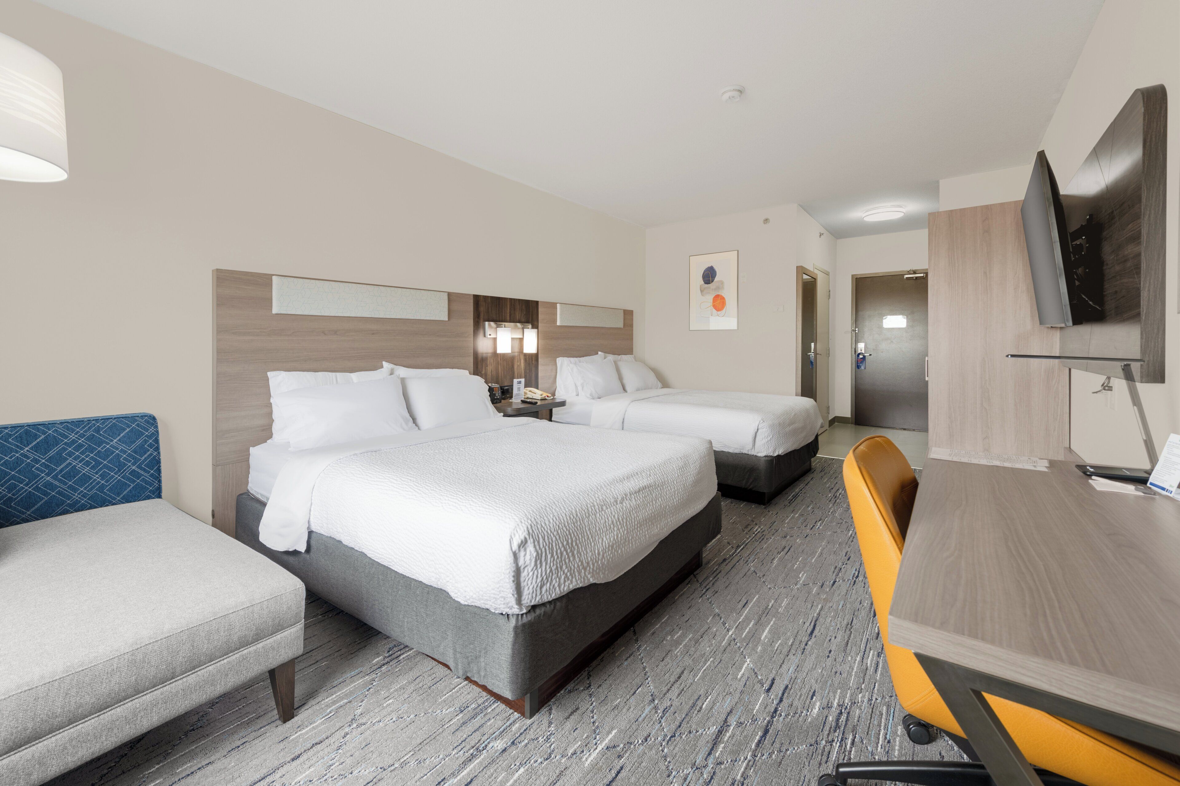 Una habitación de hotel con dos camas, un escritorio, una silla, un televisor y un baño.