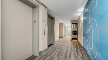 Un pasillo de hotel con pisos alfombrados, una pared azul con diseño geométrico y vista a una zona de cocina.