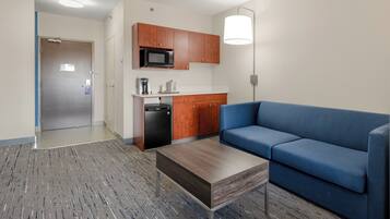 Una sala moderna con un sofá azul, una mesa de centro de madera y una kitchenette con microondas.