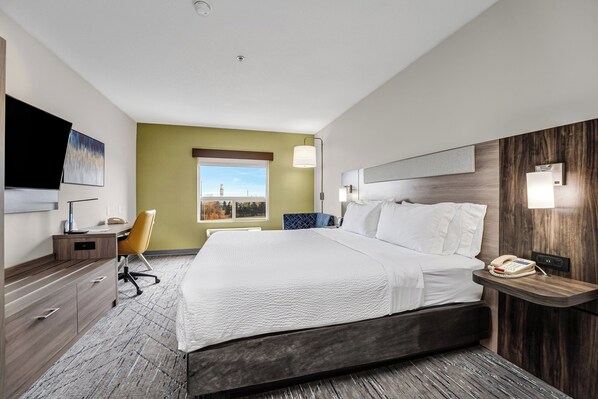 A modern hotel room with a large bed, a desk with a chair, a TV, and a window with a view.