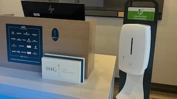 A reception desk with a digital display, a sign for Holiday Inn Express & Suites, and a hand sanitizer dispenser.