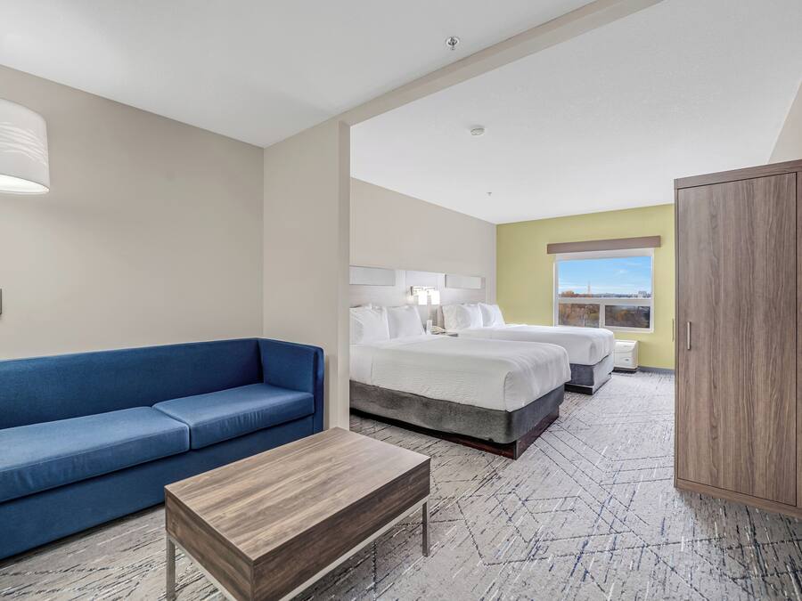 Una habitación de hotel moderna con un sofá azul, una mesa de centro de madera, una cama grande con dos almohadas y un armario.