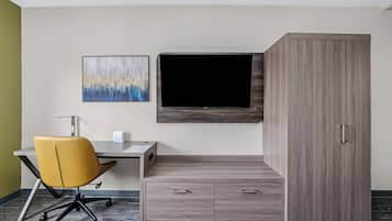 A hotel room with a desk, a yellow office chair, a TV mounted on the wall, and a wardrobe.