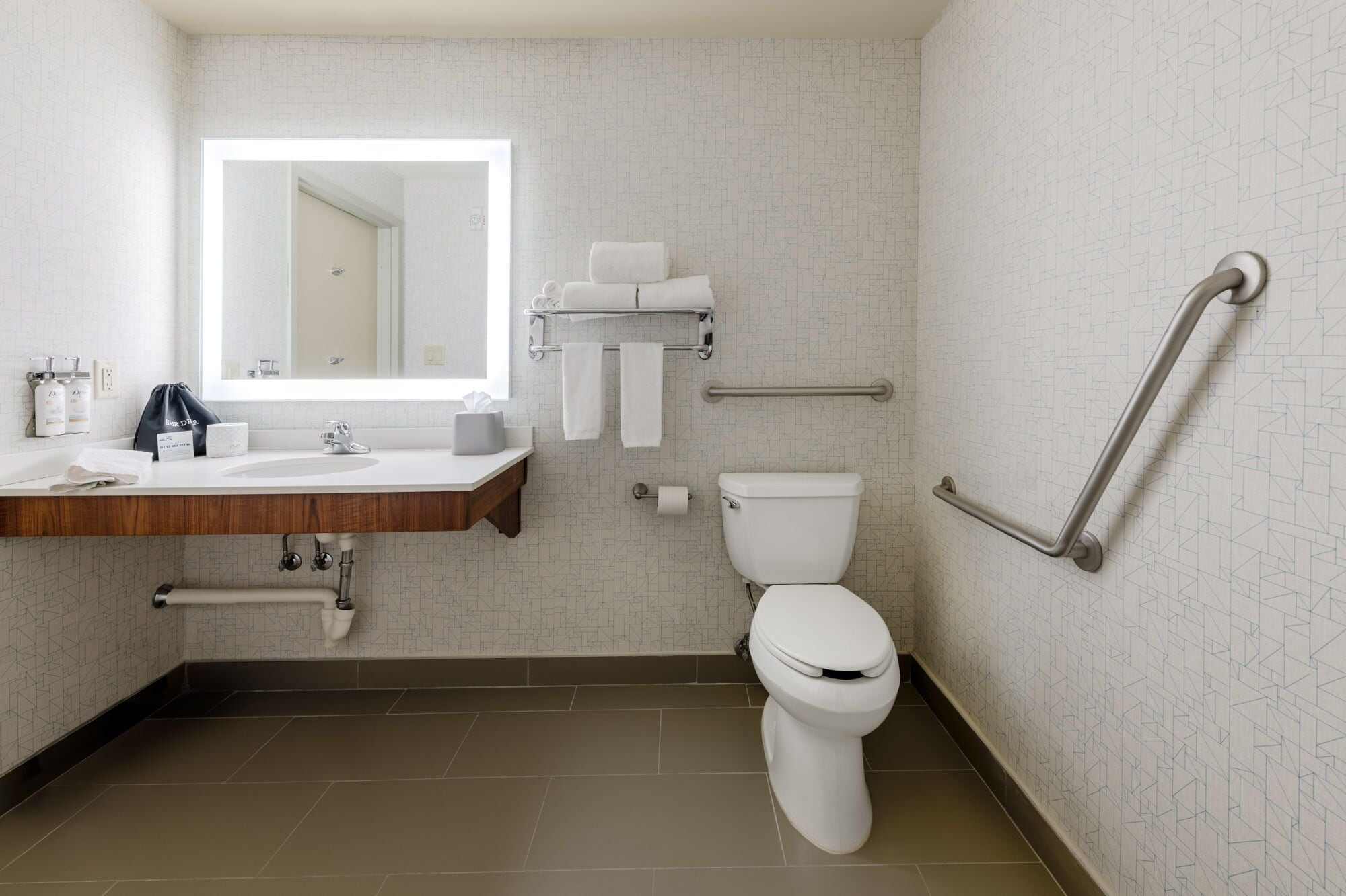 A modern bathroom with a white sink, mirror, toilet, and grab bars.