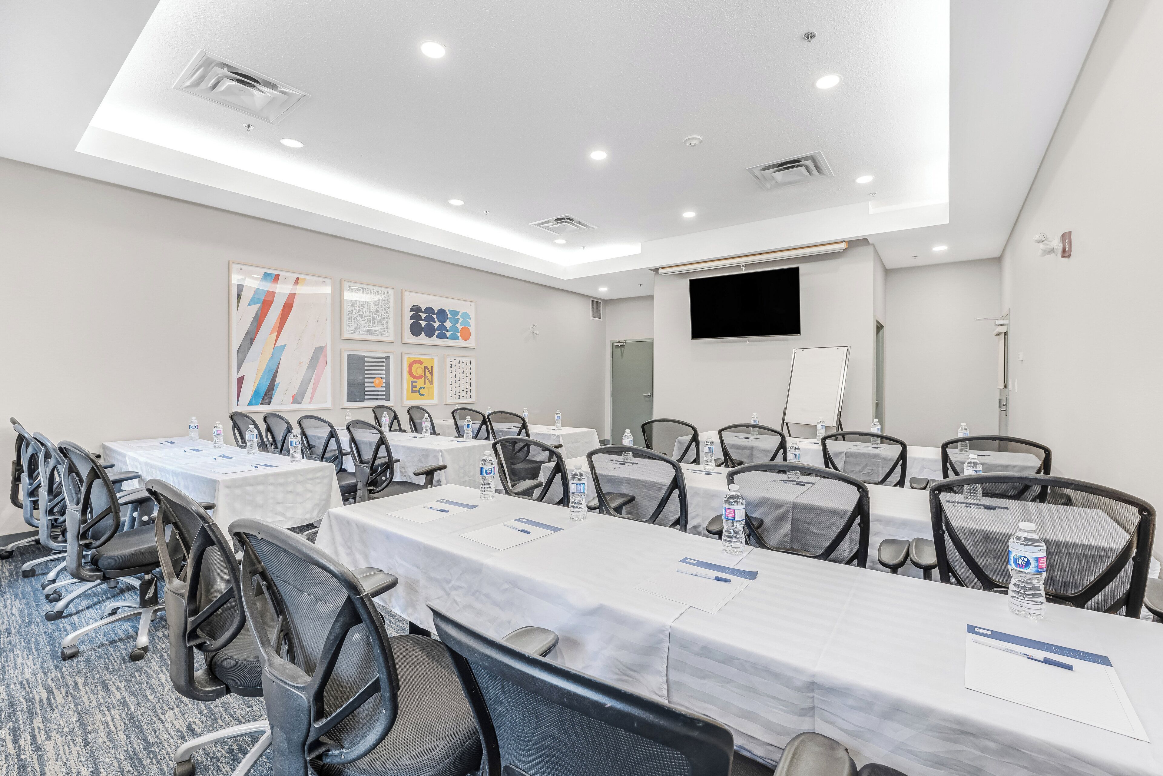 Un salón de conferencias con mesas, sillas y una pantalla para proyector.