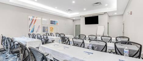 Un salón de conferencias con mesas, sillas y una pantalla para proyector.