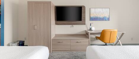 A hotel room with two beds, a desk with a chair, a TV mounted on the wall, and a painting above the desk.
