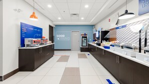 A modern kitchen area with a blue wall, a sign that says "GOOD MORNING," and a counter with various food items and appliances. - Holiday Inn Express Hotel & Suites Edmonton South by IHG (Edmonton)
