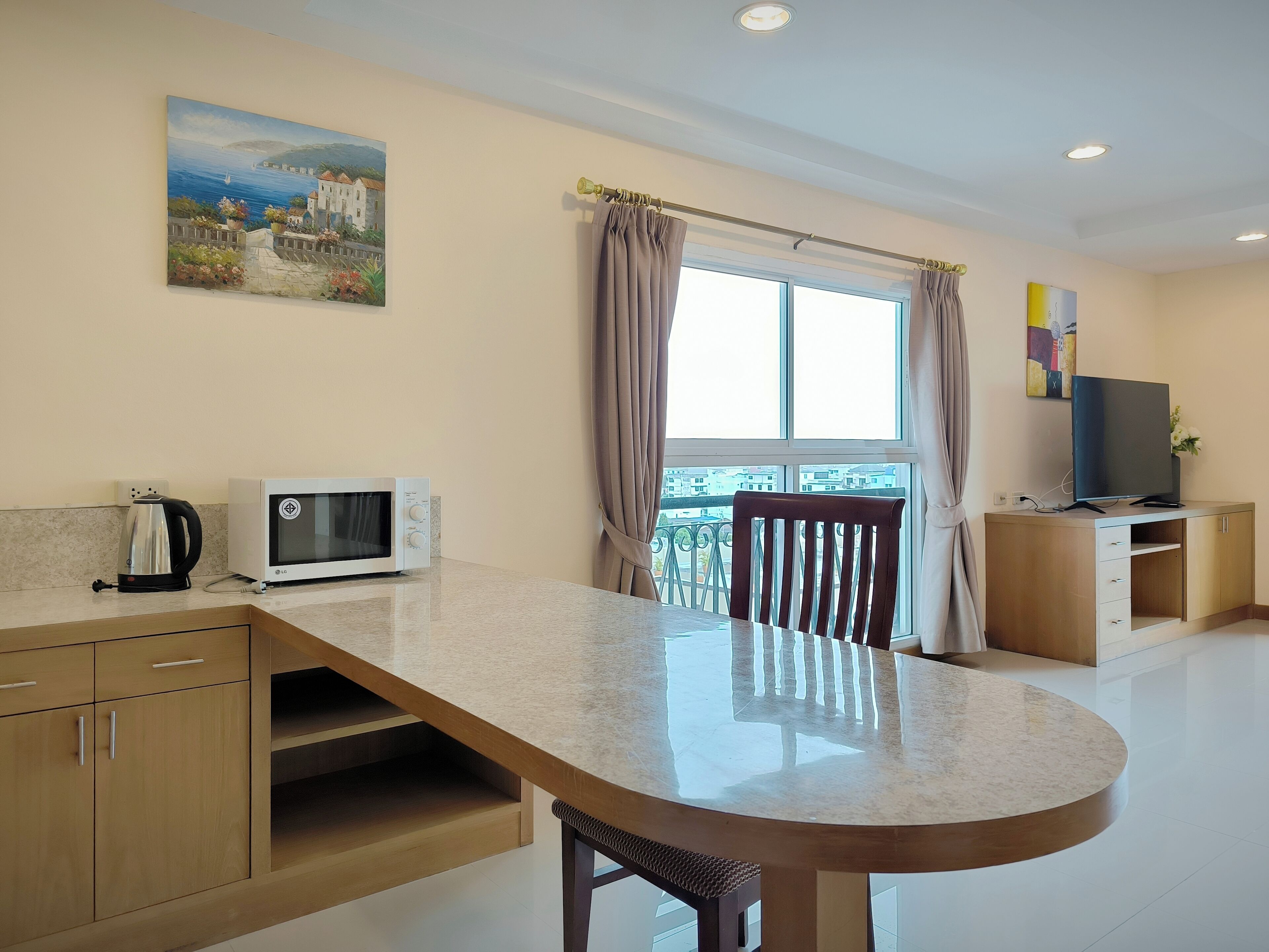 Una cocina moderna con una mesa de comedor, microondas, tetera y televisor sobre un mueble de madera.