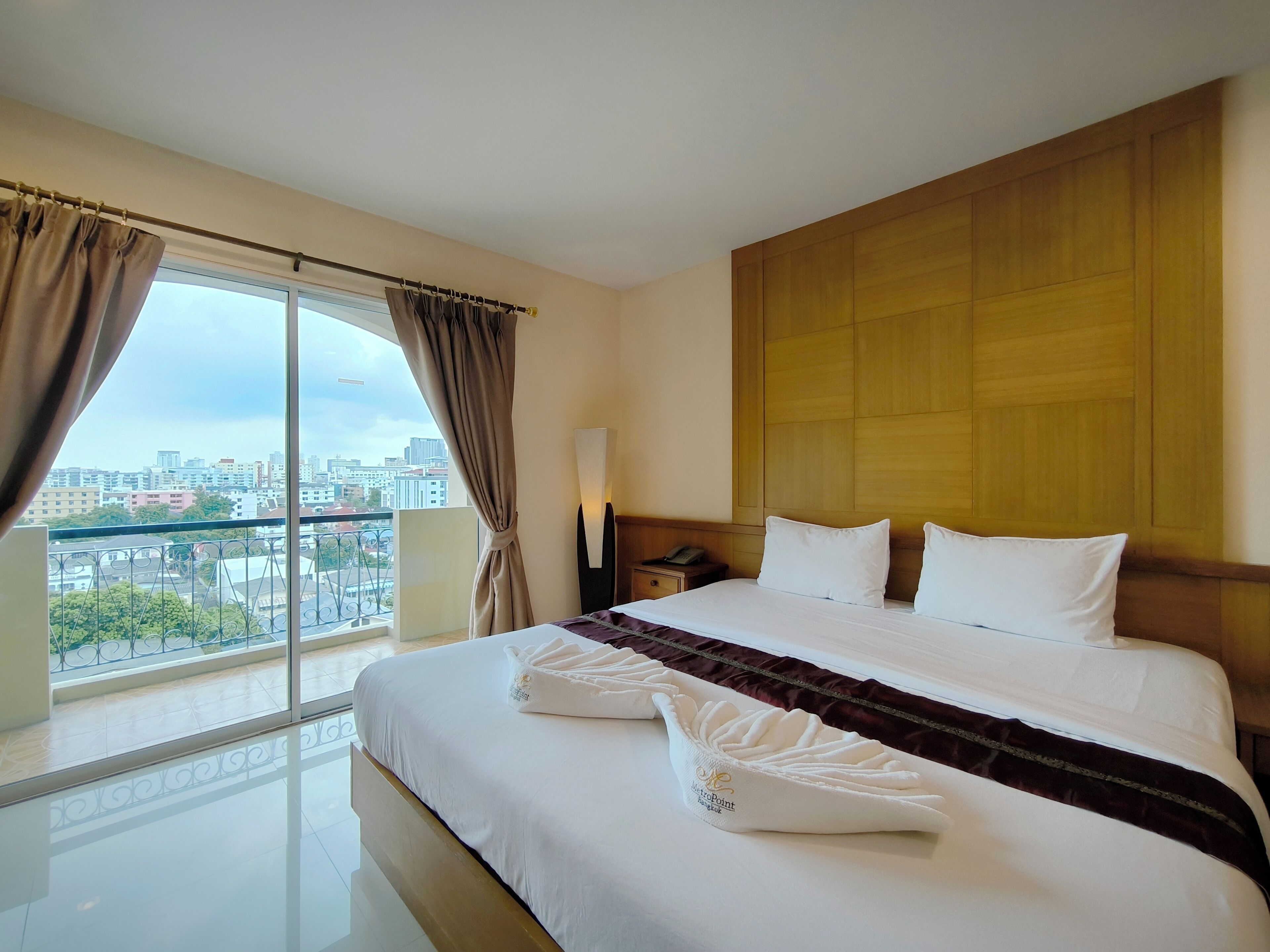 A hotel room with a large bed, a view of the city, and a wooden headboard.