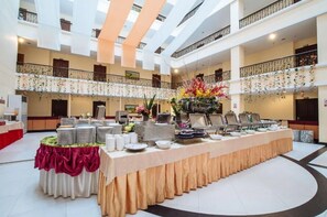 Un amplio atrio con una larga mesa de buffet, varios balcones y arreglos florales decorativos.