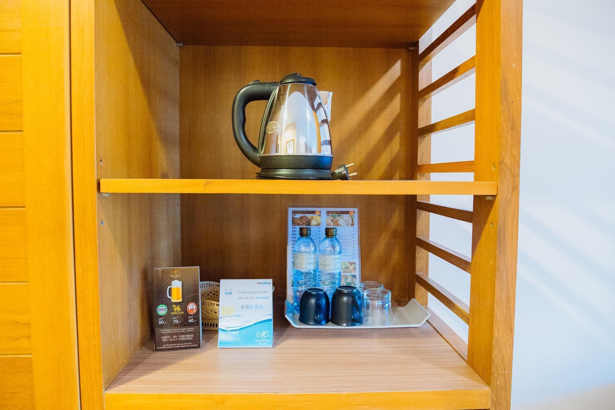 A wooden shelf with a kettle, a water bottle, and a complimentary water sign.