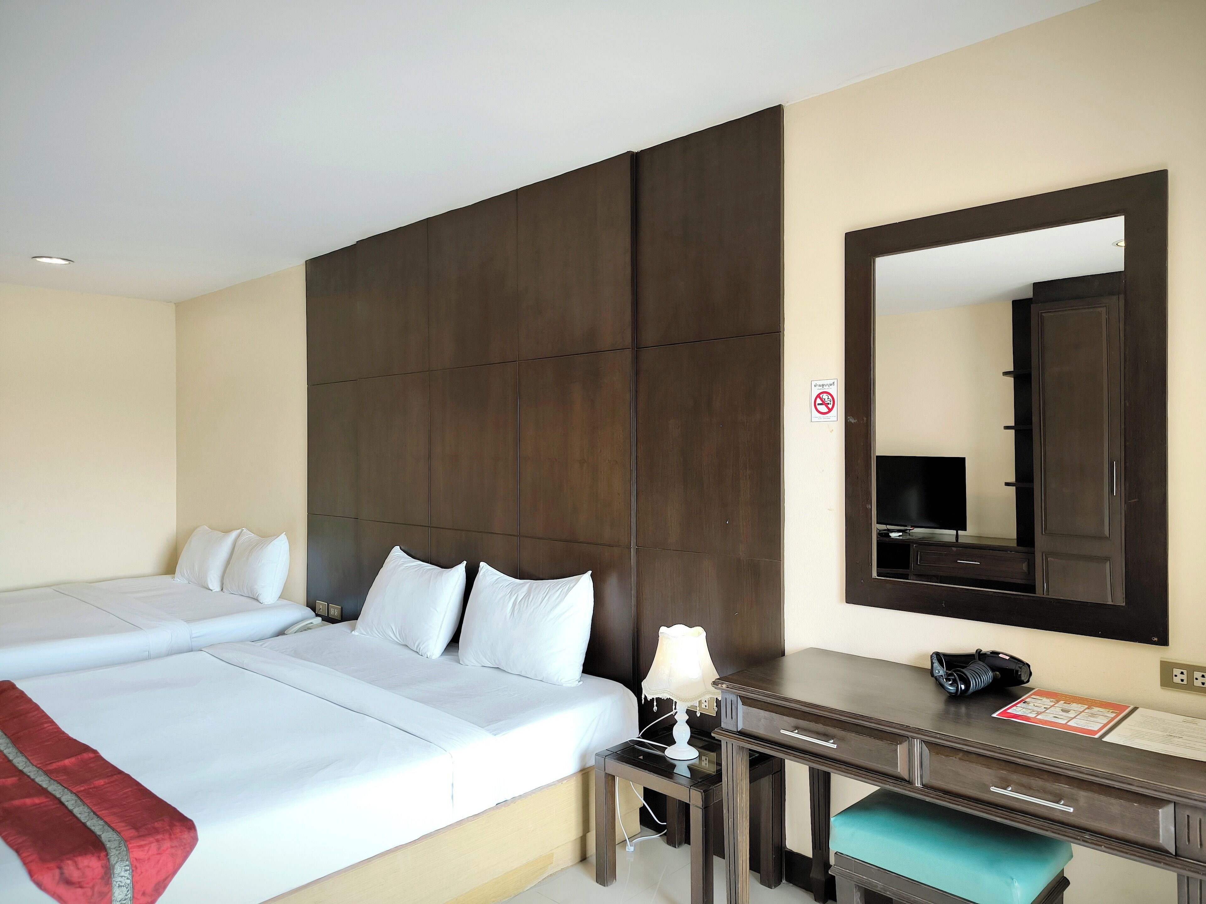 Een hotelkamer met een groot bed, een bureau met lamp, een spiegel en een televisie.