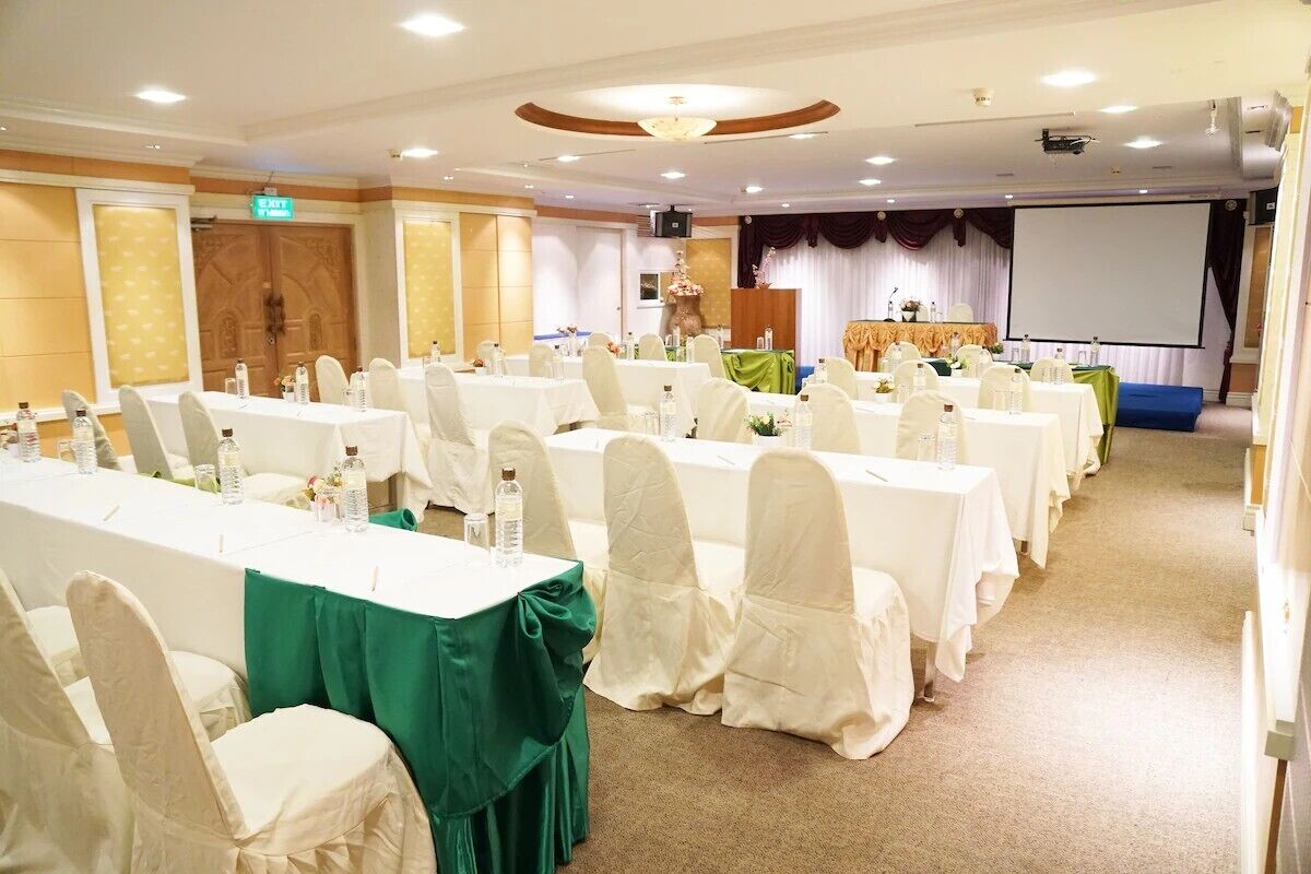 A conference room with multiple tables and chairs, a projector screen, and a stage with a podium.