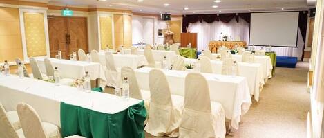 A conference room with multiple tables and chairs, a projector screen, and a stage with a podium.