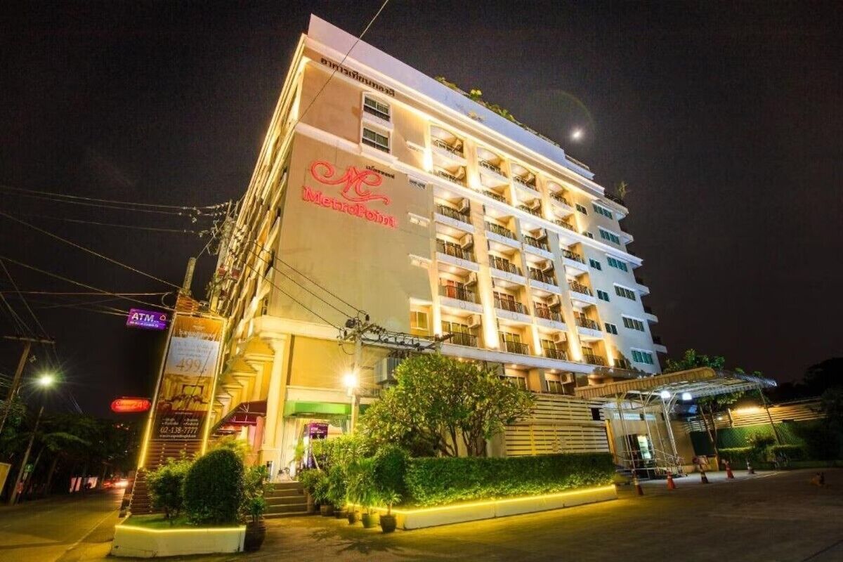 Un hotel de varios pisos con un letrero llamativo, un acceso cubierto y un área ajardinada al frente.