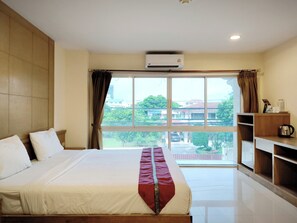 Habitación de hotel con una cama grande, una ventana con cortinas, un escritorio pequeño con un hervidor de agua y vistas a edificios y zonas verdes.