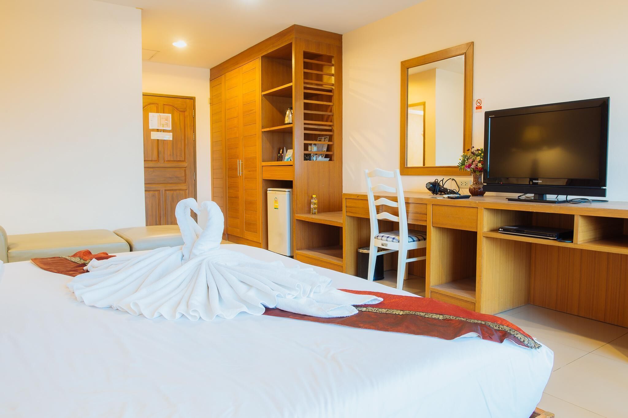 Une chambre d’hôtel avec un lit bien fait, une armoire en bois, un bureau avec une chaise, une télévision et un miroir.