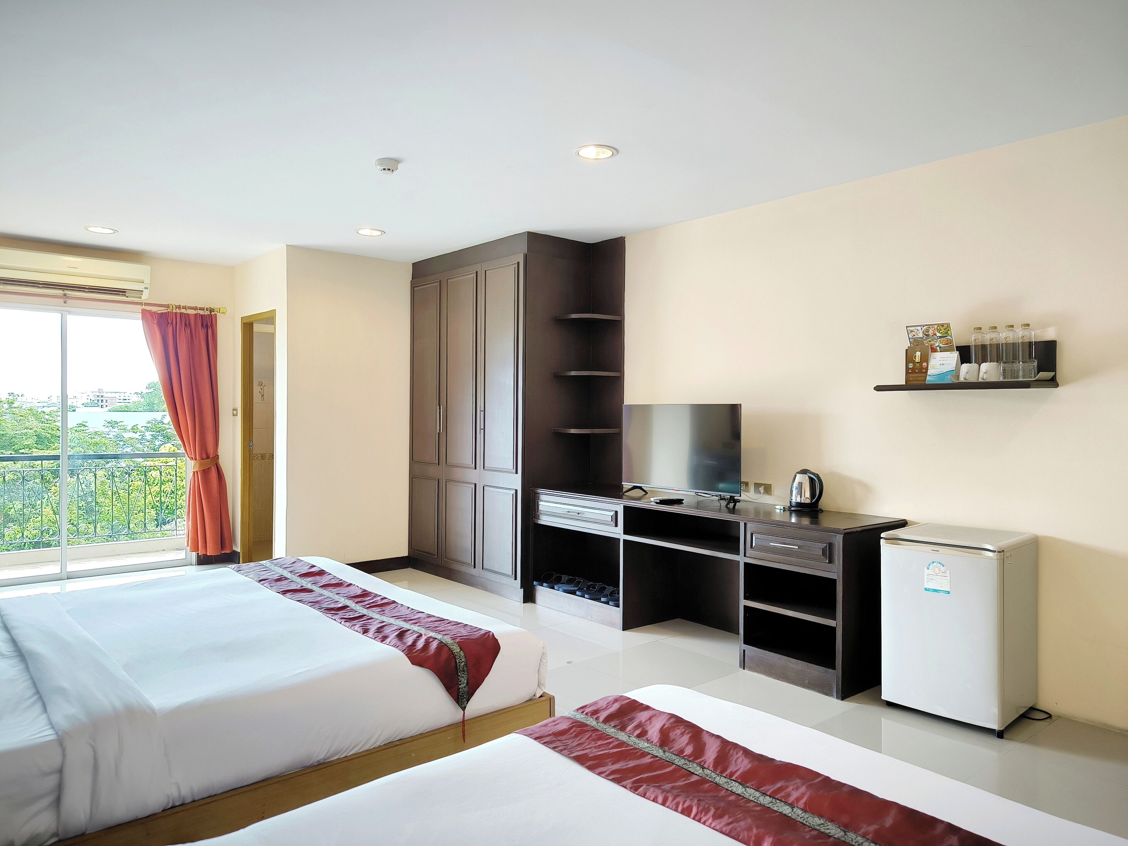 Habitación de hotel con dos camas, un escritorio con televisor, un mini refrigerador y un estante con artículos de aseo.