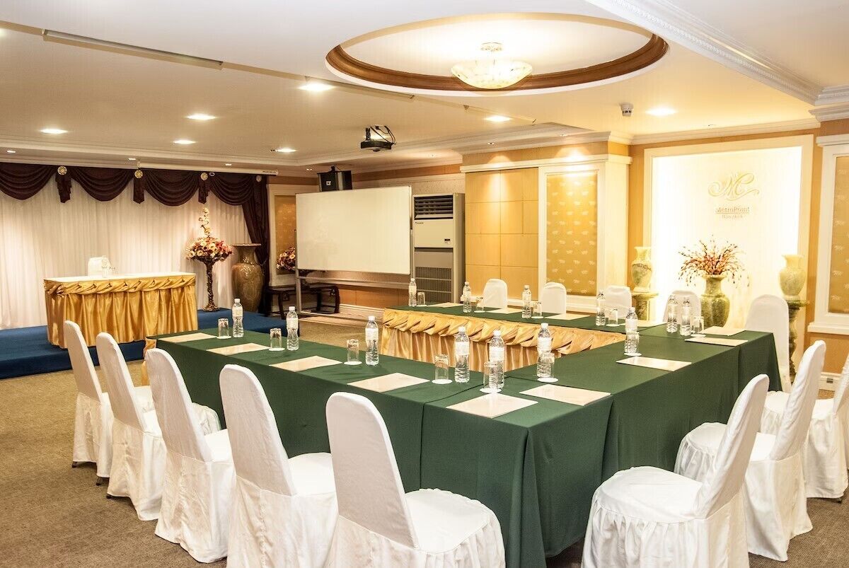 Une salle de conférence avec une longue table, des chaises blanches et un écran de projection.
