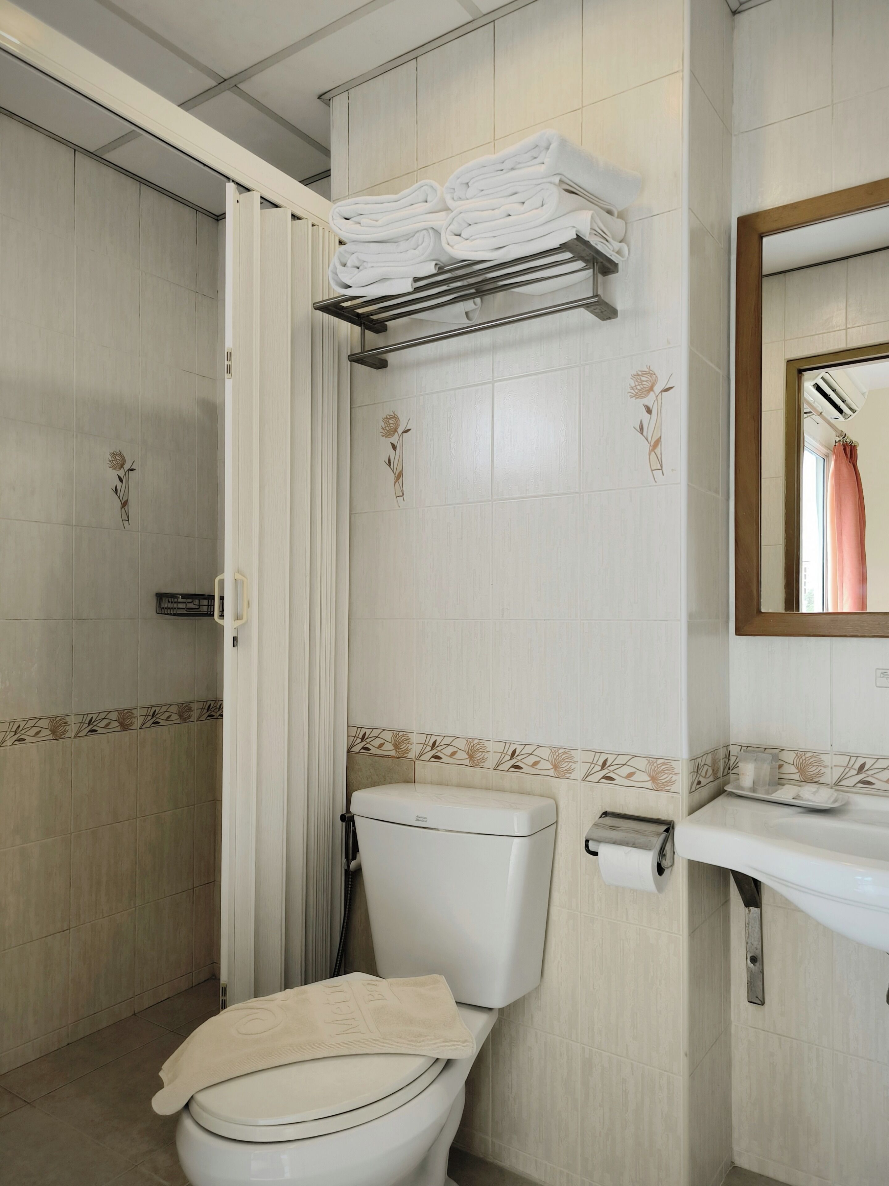 A bathroom with a toilet, a towel rack, a shower, and a sink with a mirror.