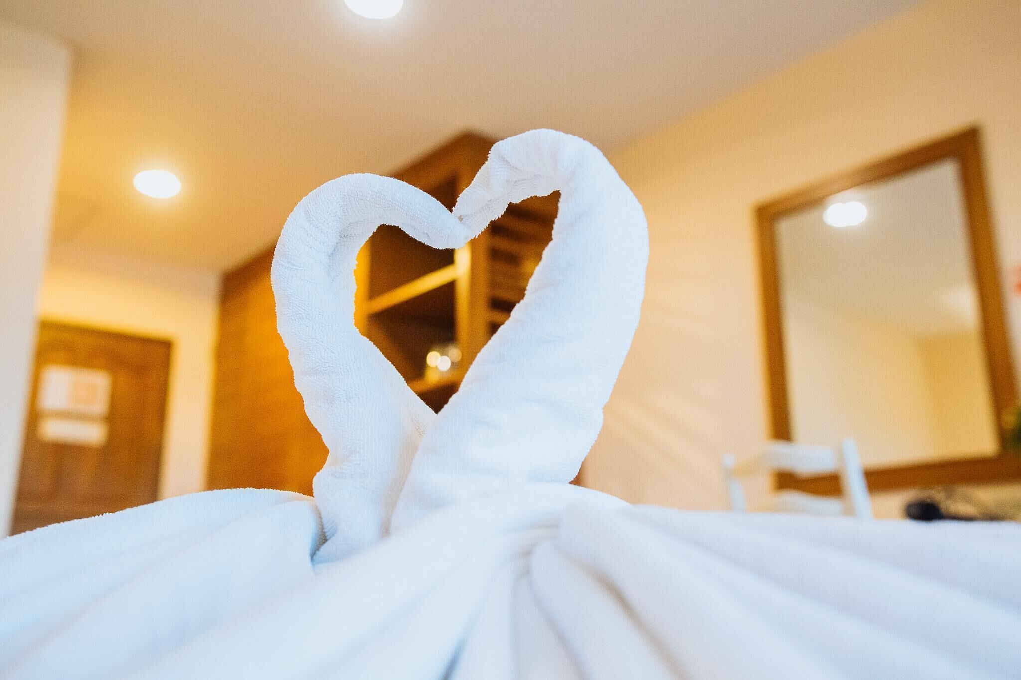 A hotel room with a bed covered in white towels arranged in a heart shape.