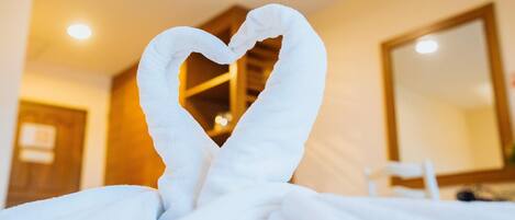 A hotel room with a bed covered in white towels arranged in a heart shape.