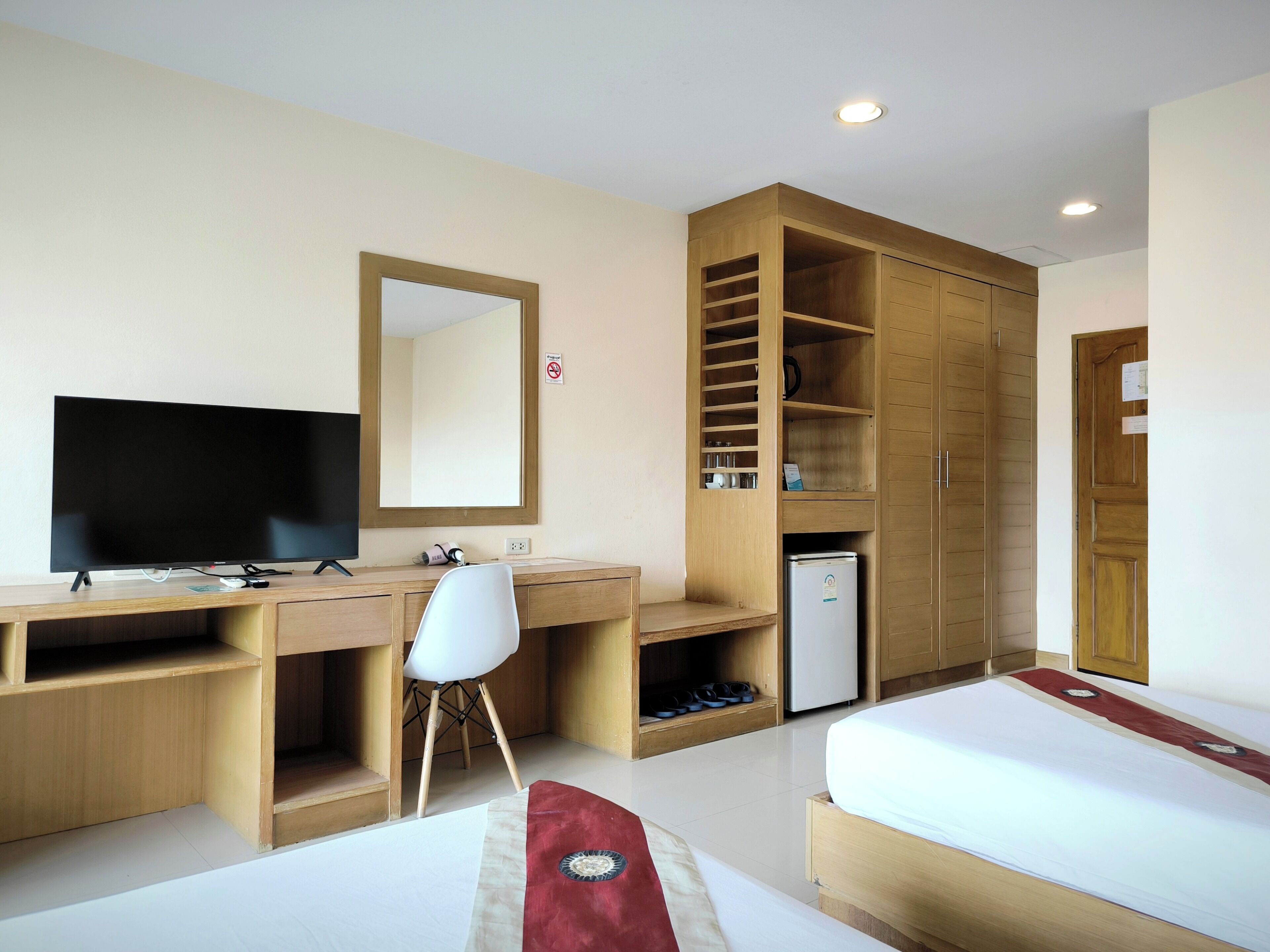 Een hotelkamer met een houten bureau, een televisie, een witte stoel, een bed en een garderobe.