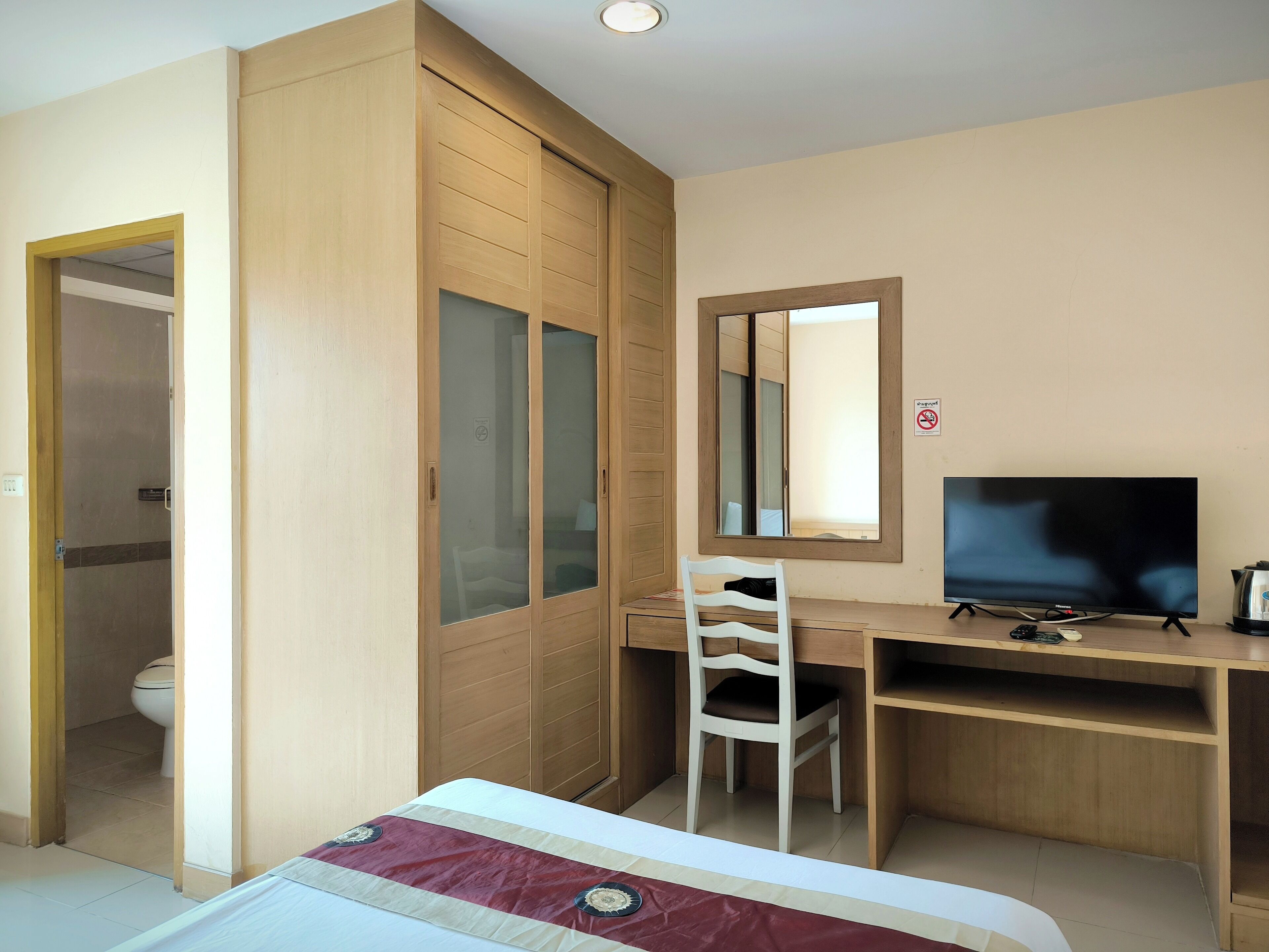 Una habitación de hotel con cama, escritorio con silla, televisor y armario con espejo.