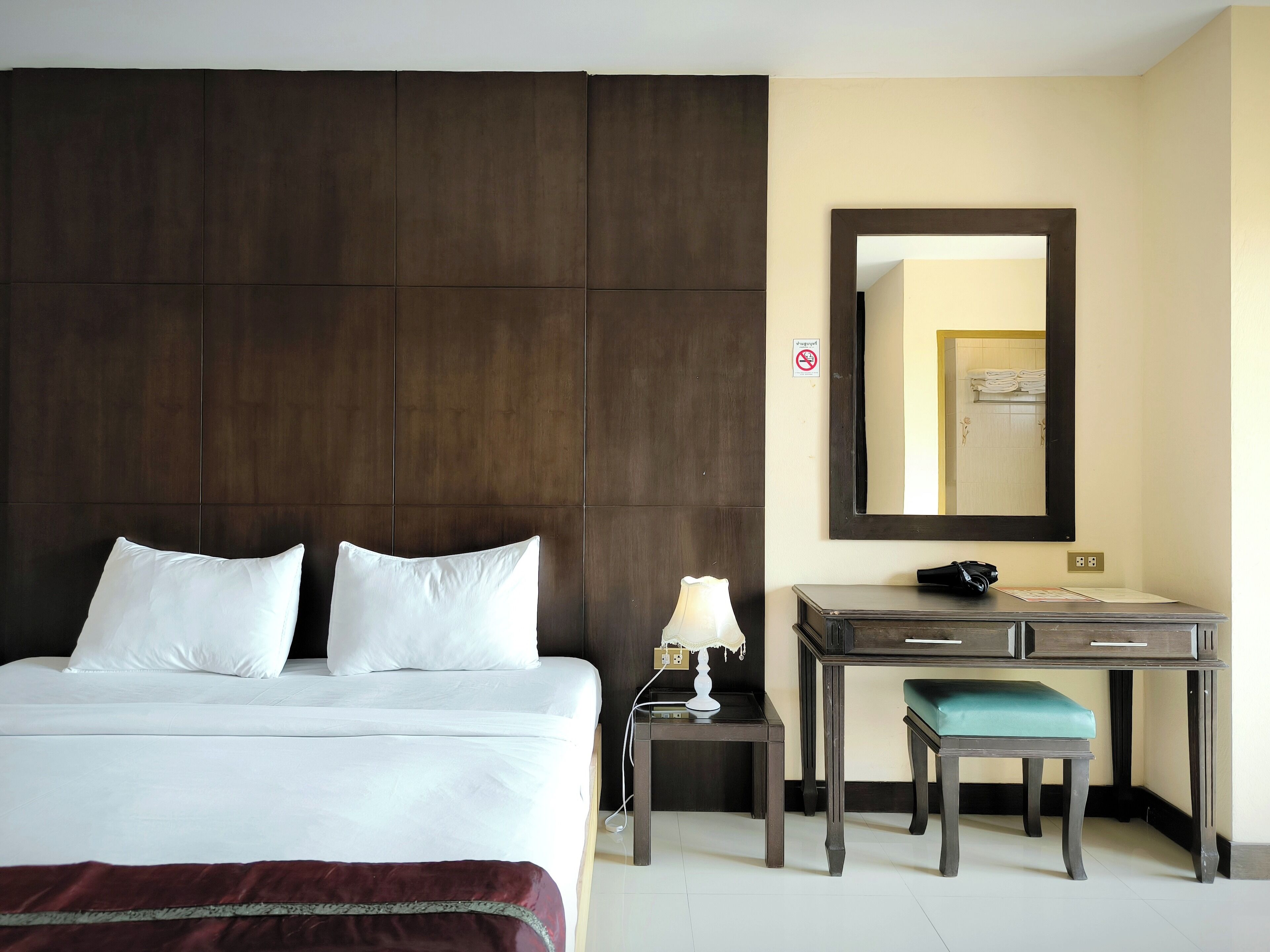 A hotel room with a large bed, a desk, a chair, a lamp, and a mirror.