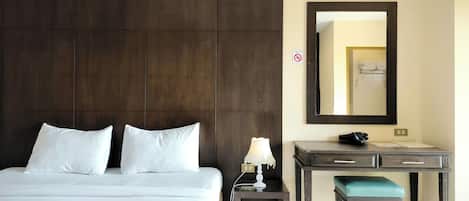 A hotel room with a large bed, a desk, a chair, a lamp, and a mirror.