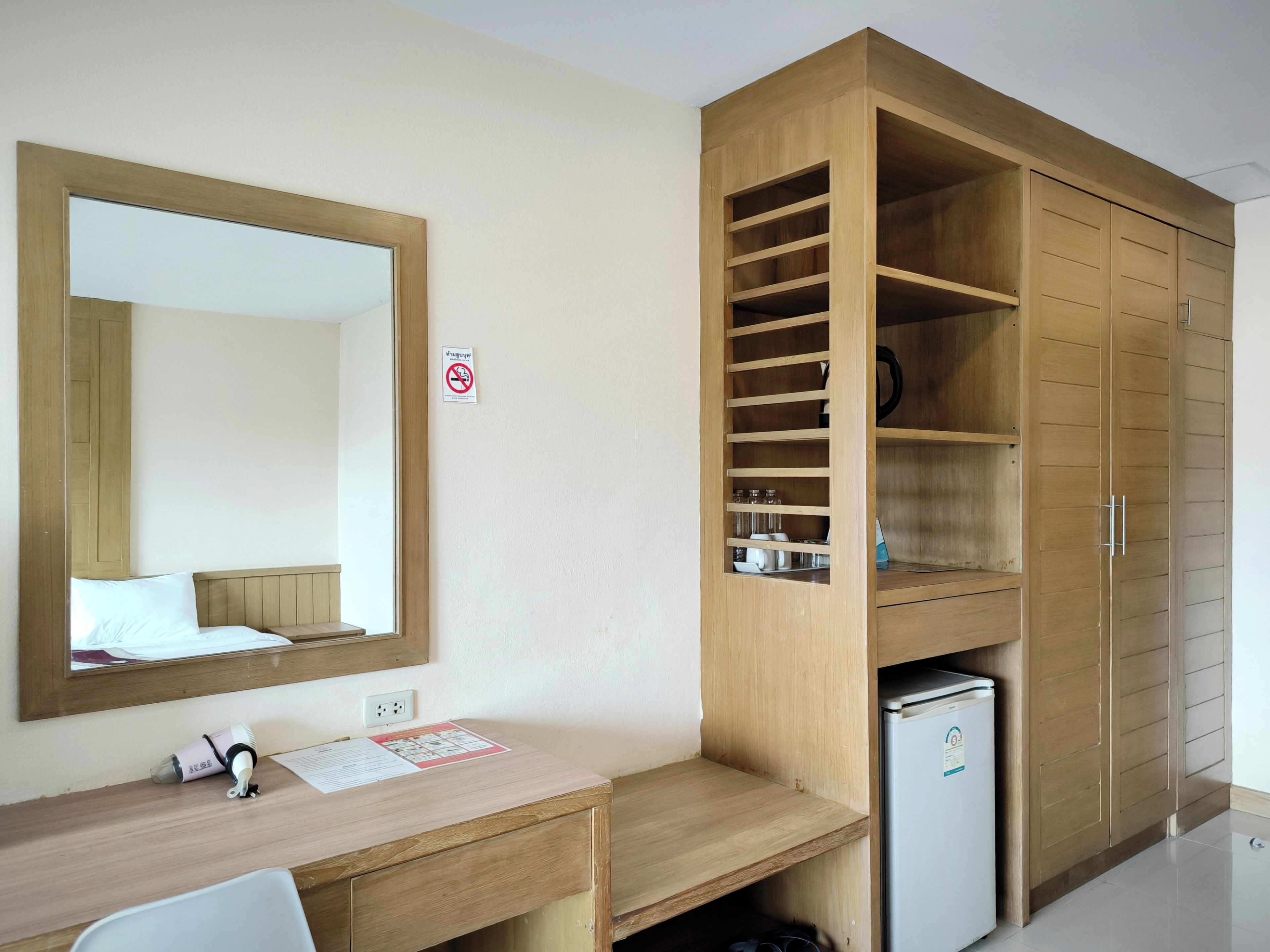 Ein Hotelzimmer mit einem Holztisch, einem Spiegel, einem Kleiderschrank mit Einlegeböden und einem kleinen Kühlschrank.