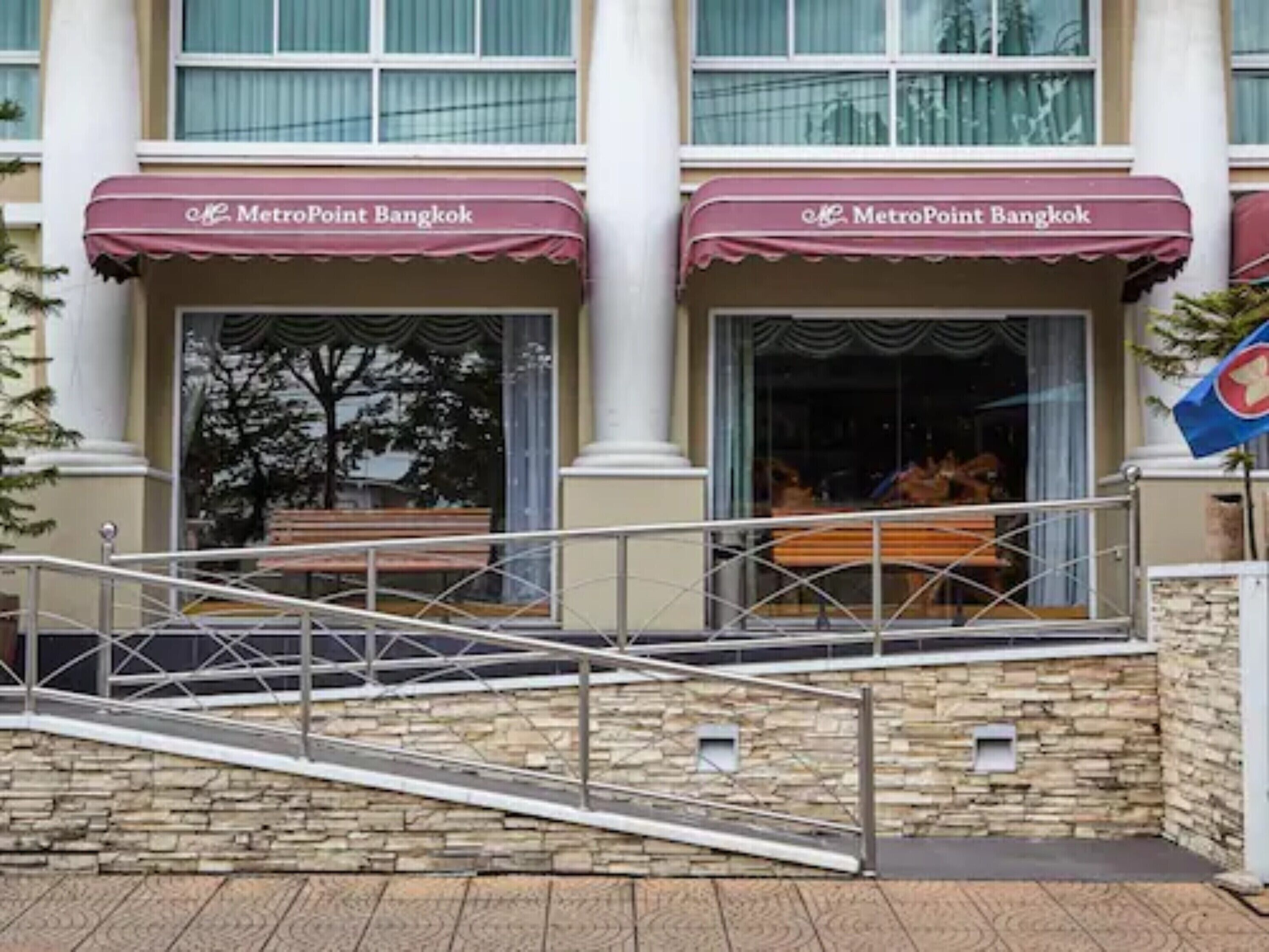 Un bâtiment doté de deux entrées, chacune surmontée d’un auvent portant l’inscription « MetroPoint Bangkok ». Un mur en pierre et un escalier métallique mènent à l’entrée.
