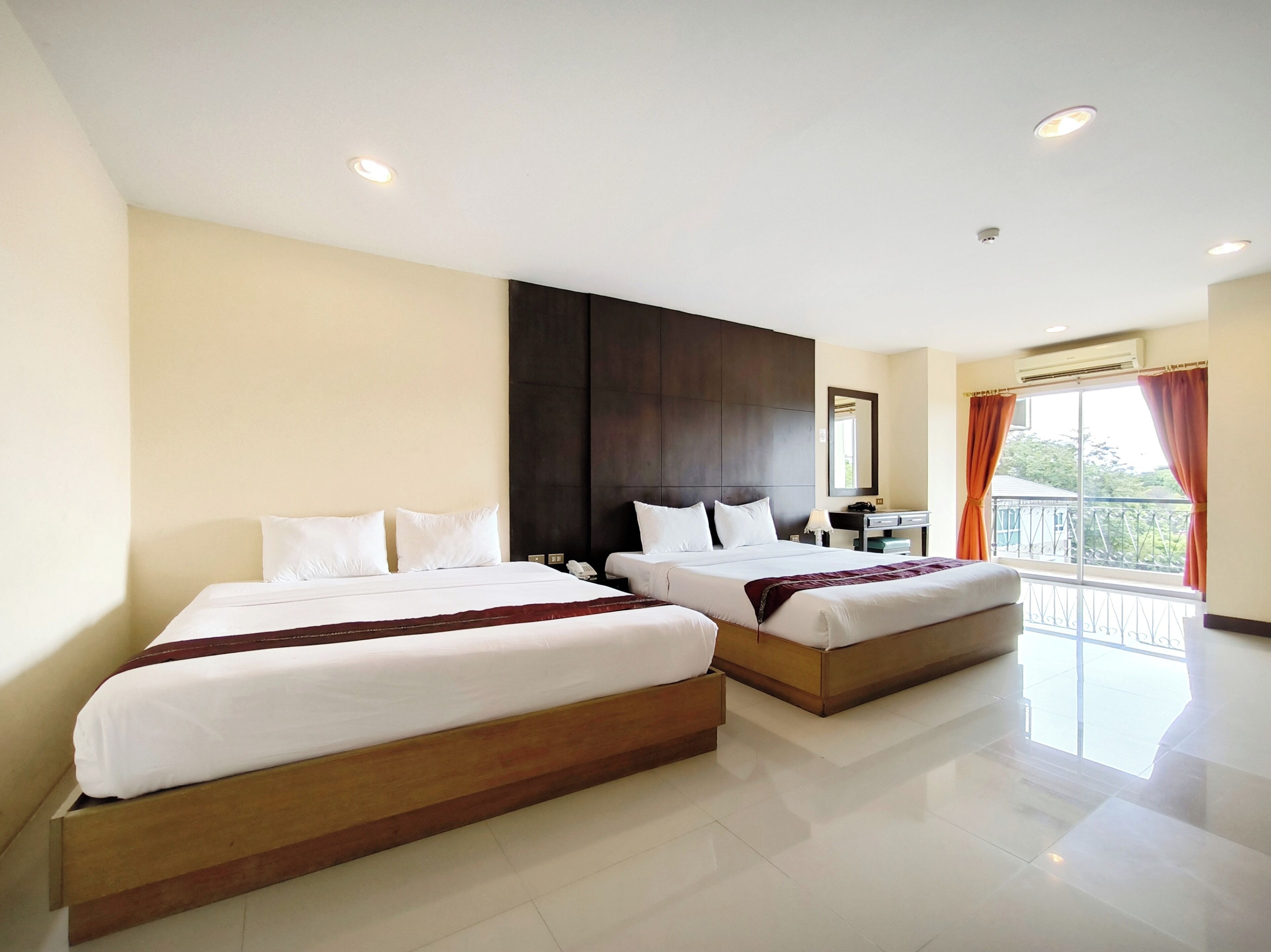 A hotel room with two beds, a large window with curtains, a desk with a chair, and a mirror on the wall.