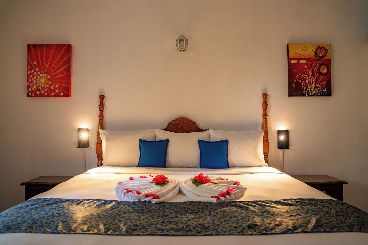 Una cama bien hecha con almohadas azules y blancas, un cabecero de madera y dos lámparas fijadas a la pared.