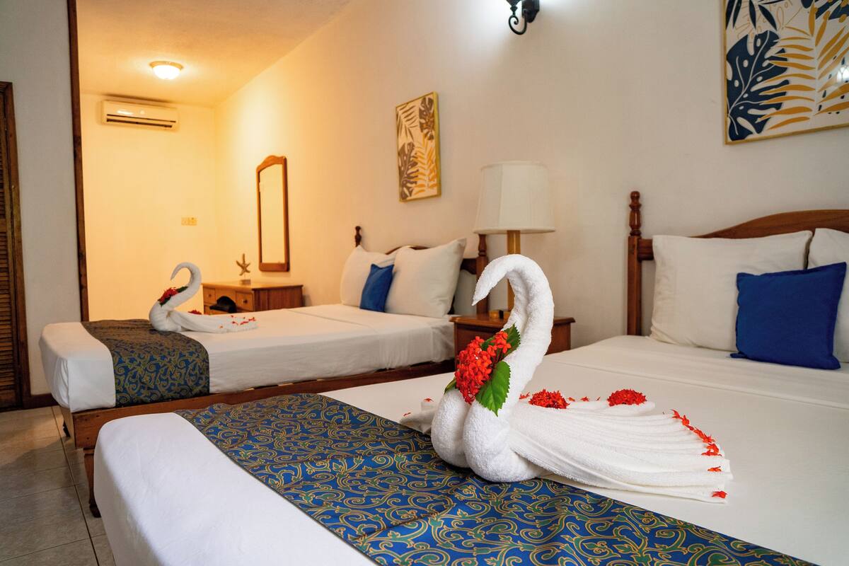 Habitación de hotel con dos camas, un espejo grande y un cisne decorativo hecho con toallas sobre la cama.