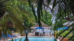 Uma área de piscina com espreguiçadeiras, um espaço de estar coberto e plantas em vasos.